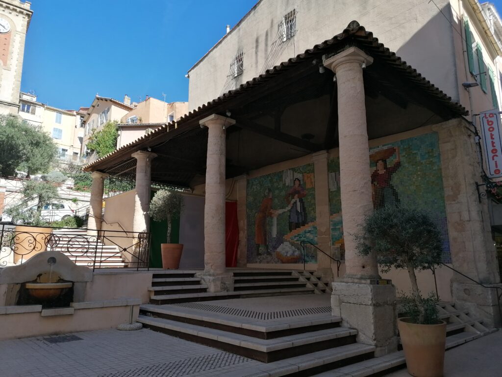 Place avec des colonnes toscanes couvertes. Sous les colonnes, fresque mosaïque représentant des lavandières. A gauche, une petite fontaine - Agrandir l'image, fenêtre modale