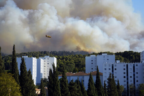 Vue du quartier du Charrel avec un feu de forêt en arrière-plan et un canadair qui survole la zone