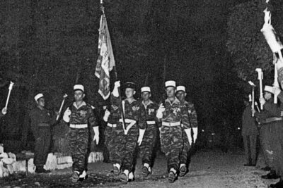 Des soldats marchent, le premier brandissant le drapeau du 1er Régiment Etranger. Autour d'eux, des soldats forment une haie et tiennent des flambeaux - Agrandir l'image 2 sur 2, fenêtre modale