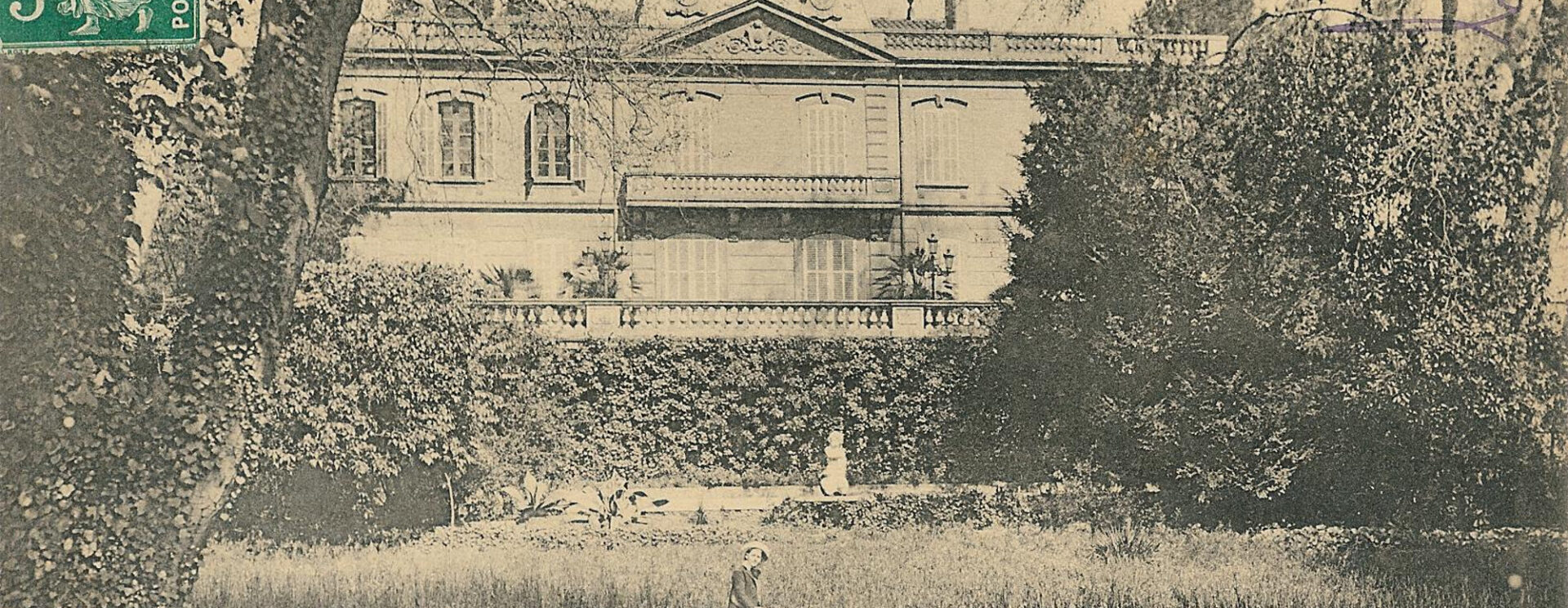 Au premier plan le jardin où pose une jeune femme, au second plan la façade du château en hauteur par rapport au jardin.