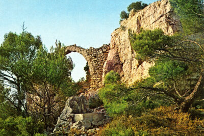 Photo en couleur de l'arche d'entrée du village d'Aubignane entre les pins. - Agrandir l'image 18 sur 18, fenêtre modale