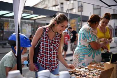 Des personnes, dont une jeune femme très souriante, regardent l'un des étals du marché des créateurs sur le cours Foch descendant, le 28 juin 2024 - Agrandir l'image, fenêtre modale