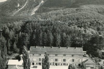 Vue en hauteur d'une grande bastide de 3 étages avec 7 fenêtres à chaque étage et une aile de chaque côté. Au fonds, la forêt et une haute montagne. - Agrandir l'image 17 sur 18, fenêtre modale