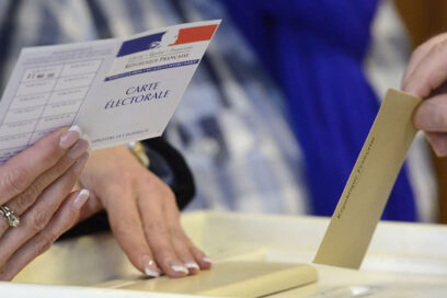 Une main portant un bulletin de vote s'apprête à le déposer dans une urne. - Agrandir l'image, fenêtre modale