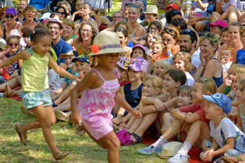 Spectacle de Fesimôme où 2 petites filles se font courser par le comédien, devant un public nombreux assis dans l'herbe