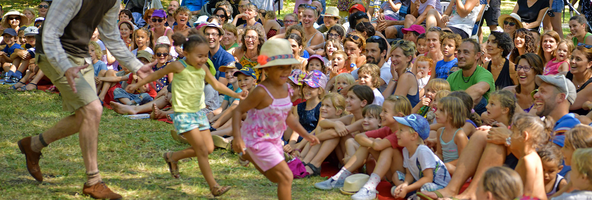 Spectacle de Fesimôme où 2 petites filles se font courser par le comédien, devant un public nombreux assis dans l'herbe