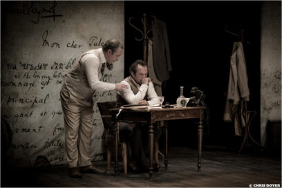 Un homme debout se penche vers un autre homme, assis sur une chaise et devant un bureau, pour lui parler - Agrandir l'image, fenêtre modale