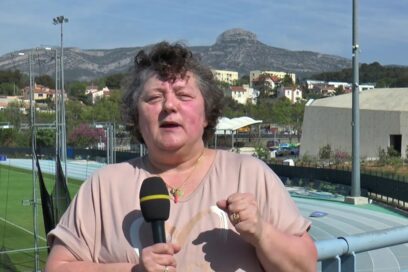 Brigitte Amoros tient un micro den interview, vue sur le Garlaban en arrière-plan - Agrandir l'image, fenêtre modale