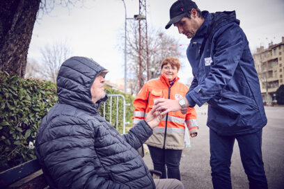 Une personne du CCAS d'Aubagne et une autre de la Croix-Rouge distribue une boisson chaude à un sans domicile fixe sur un banc - Agrandir l'image, fenêtre modale