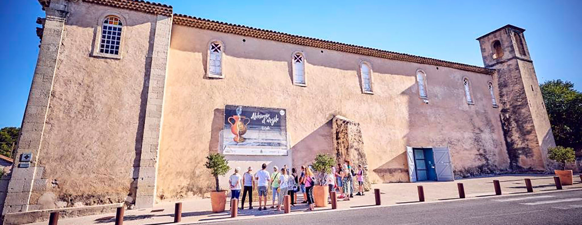Un groupe de personnes à l'extérieur du centre d'art contemporain des Pénitents Noirs regardent l'affiche d'une exposition