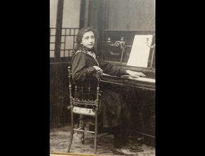 Marie-Thérèse Gras vêtue d'une robe noire, assise sur une chaise et posant devant un piano - Agrandir l'image, .JPG 276,8 Ko (fenêtre modale)
